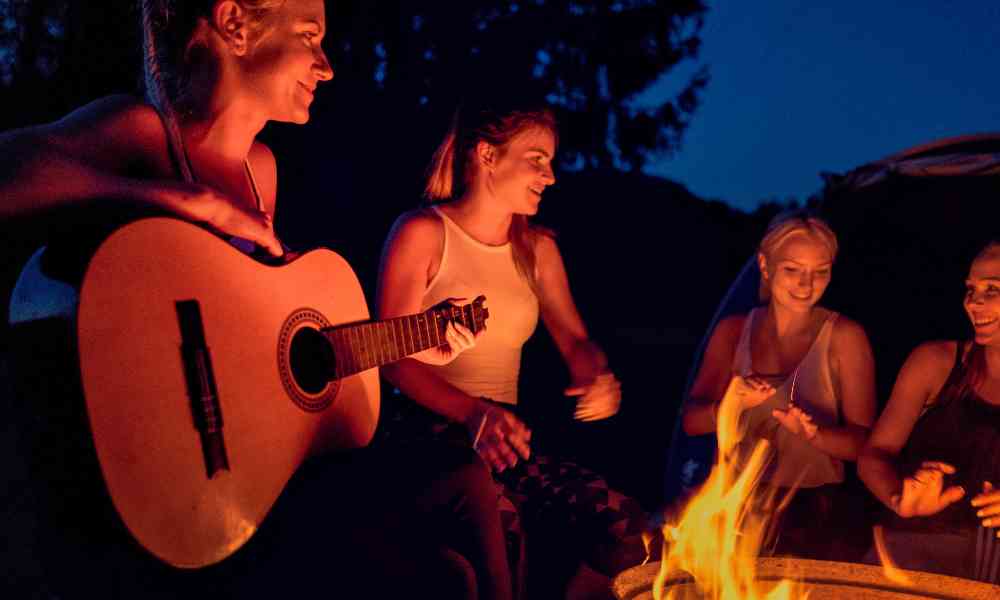 People sitting around a campfire with girl playing the guitar